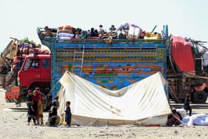 Children sit on top of a brightly coloured lorry full of personal belongings with a tent in the foreground