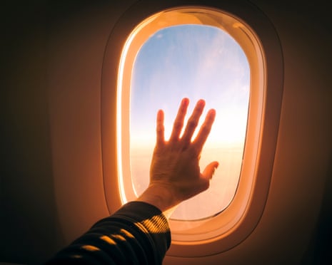 دست روی شیشه پنجرهٔ یک هواپیما که در نور غروب یا طلوع خورشید میدرخشد