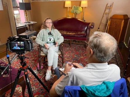 Two people sit alongside a camera on a tripod