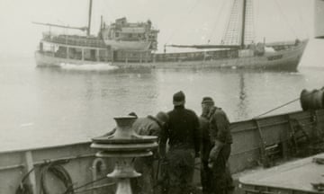 Black and white image of two people watching a ship sinking in the sea