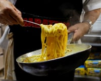 Closeup of a chef lifting sauce-covered pasta from a pan