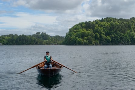 A man with grey beard rowing in a small wooden rowing boat