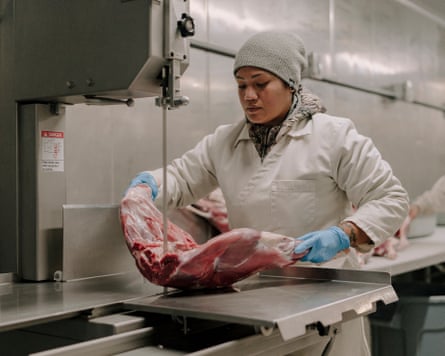 A woman cuts meat on an industrial saw.