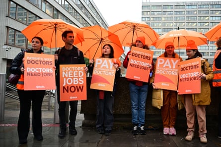 Resident doctors holding placards and orange umbrellas