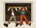Flo and Joan sit leaning back against an upright piano, hands raised to the keys above them