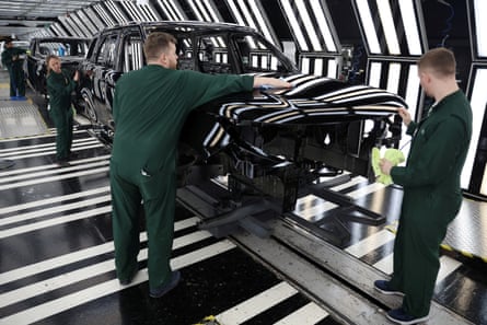 Staff in green bodysuits polish part of a black Range Rover on production line.