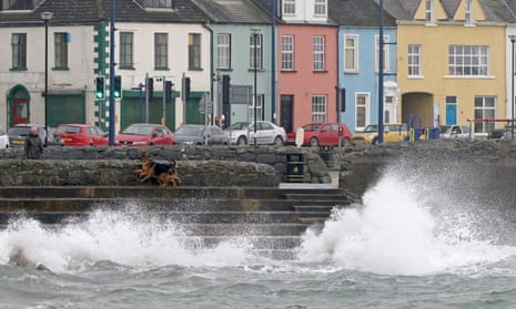 A woman walks her dogs as waves rise up on the waterfront in Donaghadee, Northern Ireland