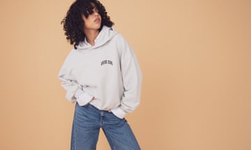 A model with curly hair wears an ecru hoodie with wide leg jeans.