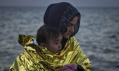 A woman wearing a thermal blanket holds her child on a beach in Lesbos