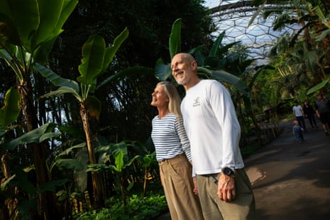Two people smiling and holding hands as they look up at tall plants