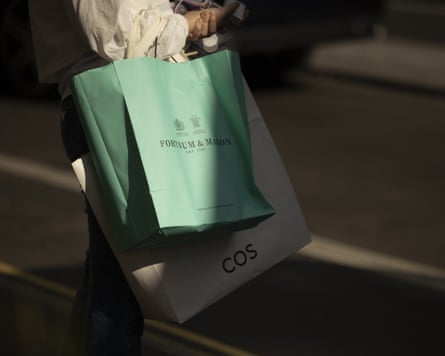 A shopper carries Fortnum and Mason and Cos bags in central London