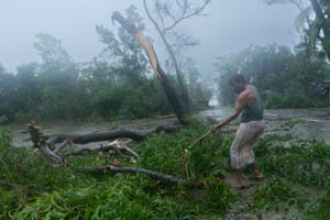 A man cuts trees and removes them while the cyclone is in progress.