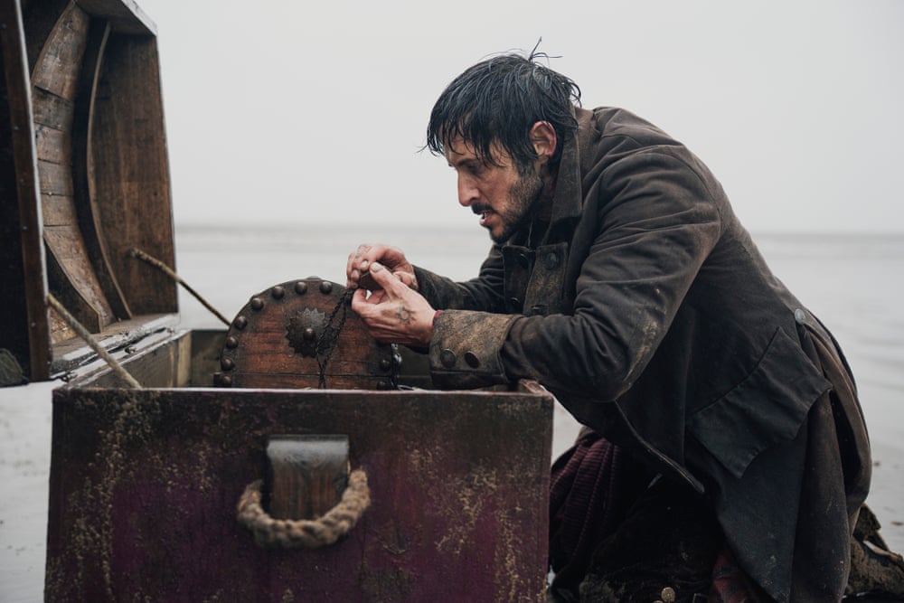 Tomer Capone as Billy Bones in Treasure Island Billy Bones played by Tomer Capone in a Treasure Island scene beside a treasure chest on a beach
