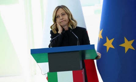 Giorgia Meloni standing at a lecturn with an EU flag to the side