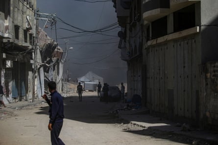 Smoke rises after an Israeli airstrike in Gaza City. A man stands in a part-ruined street as black smoke fills the sky. Tents are seen in the background