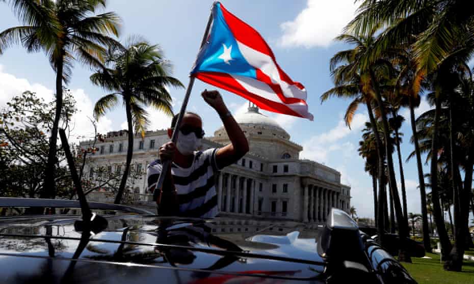 A man holds a Puerto Rican national flag during a protest against the school reopening this week. Over the past half century Puerto Rico has held six non-binding referendums on its status.