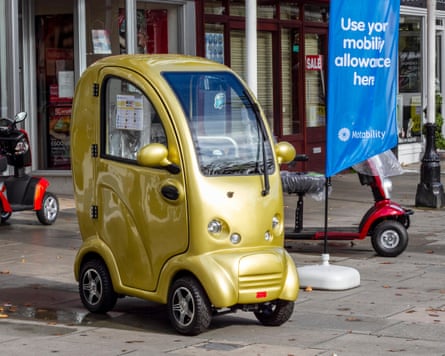 A gold electric scooter next to a sign promoting the Motability scheme
