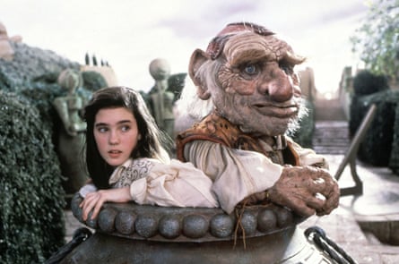 A young girl is back to back with a large, older looking puppet.