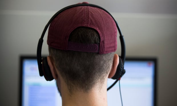 Male call centre worker wearing headset and baseball cap, seen from behind