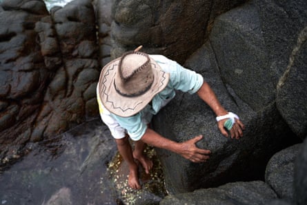A man in a sun hat climbs down rocks to a beach