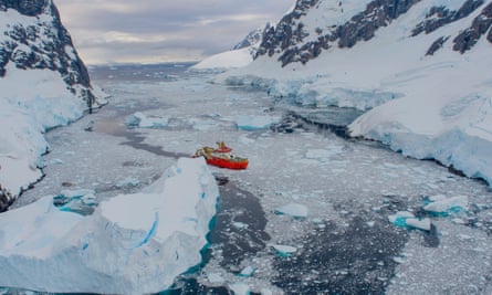 A red research ship in an icy passage of water between two land masses