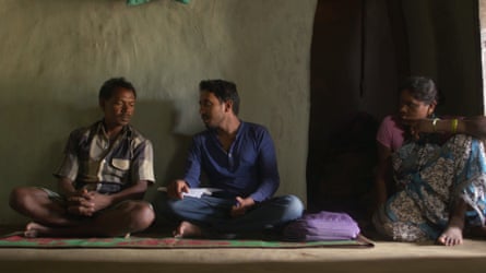 Two men and a woman sit on a mat on the floor talking