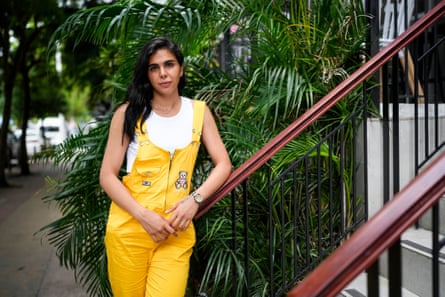 person wearing yellow overalls and white top poses against red stair railing