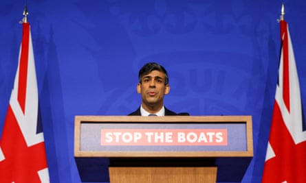 Britain’s prime minister, Rishi Sunak, is flanked by union flags. His head can be seeing looking over a lectern bearing the sign ‘stop the boats’