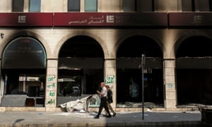 Pedestrians walk past a bank that was attacked and burned by demonstrators in Tripoli.