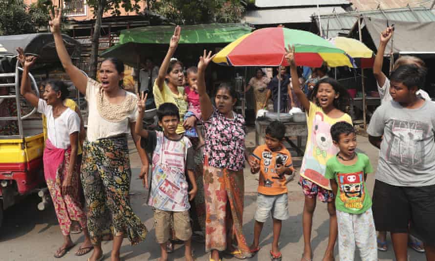 People give the three-fingered salute as they watch anti-coup protesters march past in Mandalay
