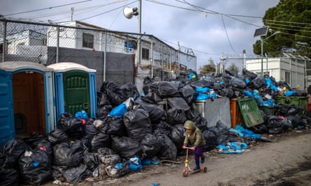 A boy plays with a scooter in front of rubbish bags in area outside camp Moria.