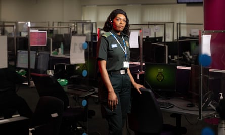 Laura Davis, call assessor for the West Midlands Ambulance Service, in uniform and wearing headphones, standing by her desk