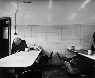 A furnace keeper slumps over a table in a tiled, worn ironworks mess room