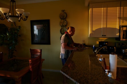 Rays from the setting sun illuminate an unlighted hotel room, in the center of which stands a middle-aged man with his long hair pulled into a bun at the back of his head.