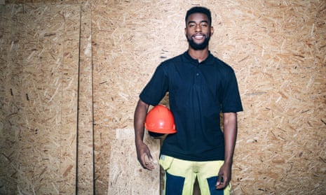 Portrait of confident carpentry student holding hardhat while standing against wooden wall“”