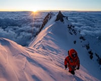 A woman wearing heavy mountaineering gear walking on a snow-covered mountain