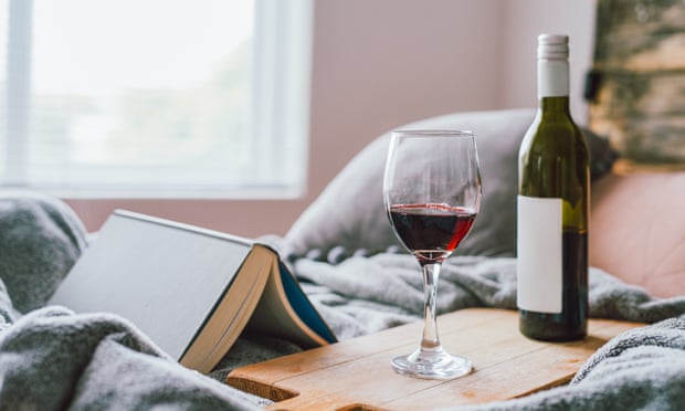 A single glass of red wine, and half empty bottle and a book on a bed in a home