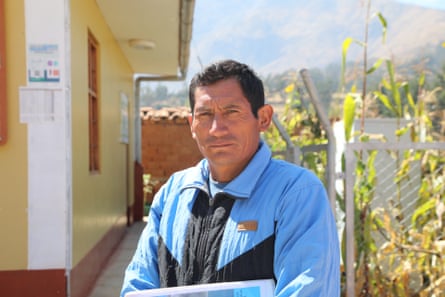 A middle-aged man in a zip-up top stands next to a building and looks at the camera