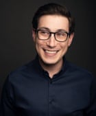 A portrait of Josh Zimmerman wearing a dark blue shirt and glasses