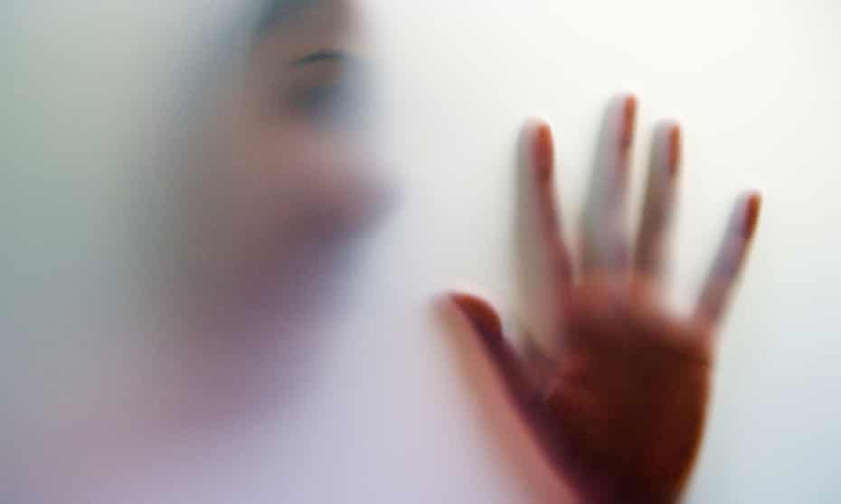 Shadowy figure of a young woman with face and hand held up against a glass door