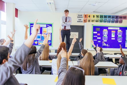 Mr Geary stands on a desk facing a group of students with their hands up