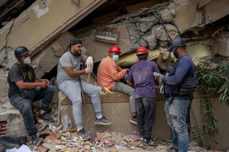 Group of men in protective equipment taking a break and sitting on a wall near a collapsed building