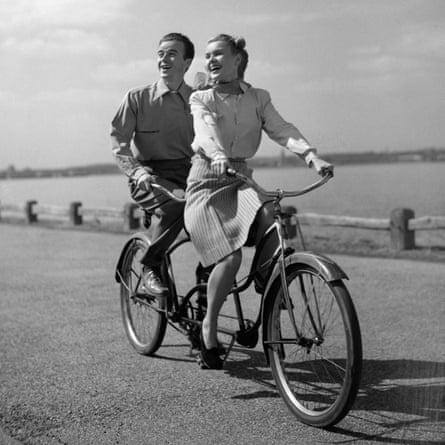 A happy 1950s couple riding a tandem bike by the sea or a lake