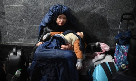 A woman holds her sleeping child while sitting on the ground at Lviv central train station