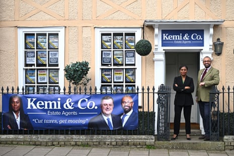 Kemi Badenoch and James Cleverly posing outside an estate agents in Essex with a banner saying "Kemi and Co" and "cut taxes, get moving".