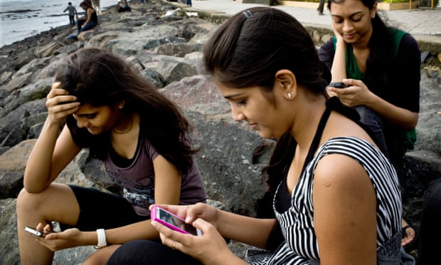 young women check their smartphones by the beach in Mumbai, India