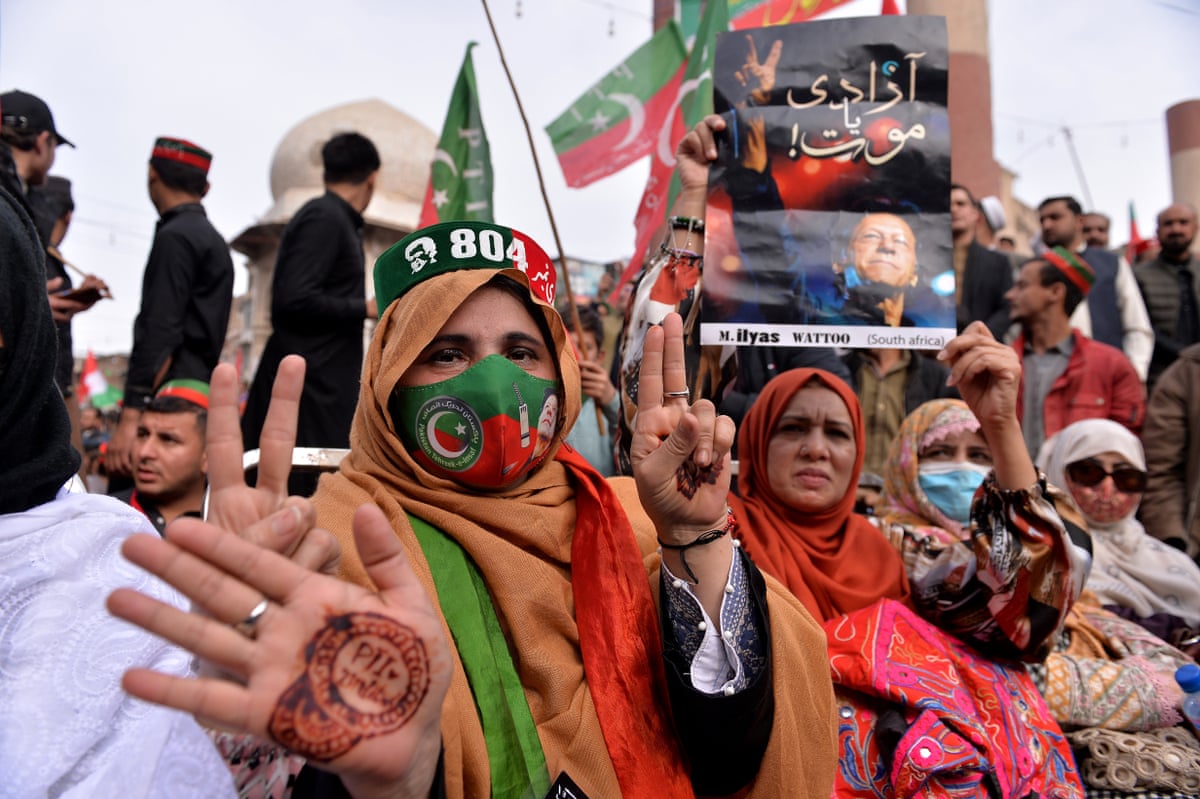 A woman holds a poster of Imran Khan while another displays a stamp on her hand while wearing a hat with the number 804 on it, which is Khan’s prisoner number