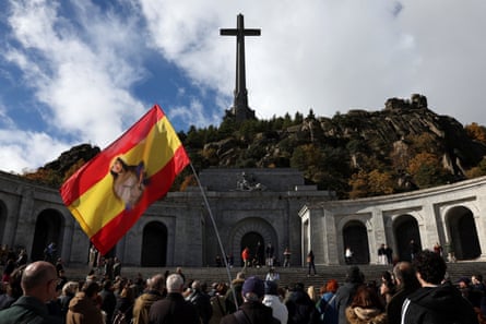 Crowds standing in front of a cross on a hill waving a flag