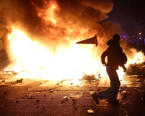 A youth flees from a fire during a protest in France. A road cone flies through the air.