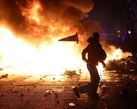 A protester throws a traffic cone past a huge blazing barricade fire at night